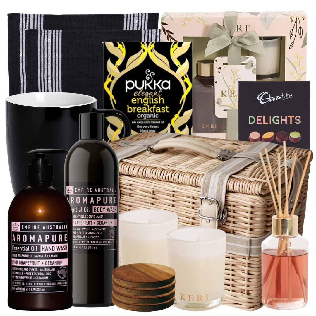 Housewarming gift basket featuring hand and body wash, a fragrance set, tea towels, wooden coasters, a mug, chocolates, and English breakfast tea