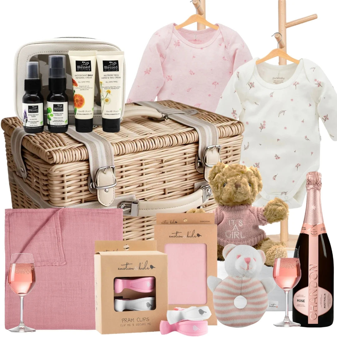 Baby gift basket with wicker basket, baby clothes, bottles, teddy bear, and other items on a white background.